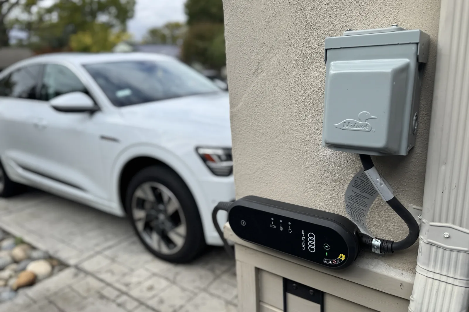 Portable EV charger plugged into a new outdoor EV charger outlet next to a parked electric car in San Jose