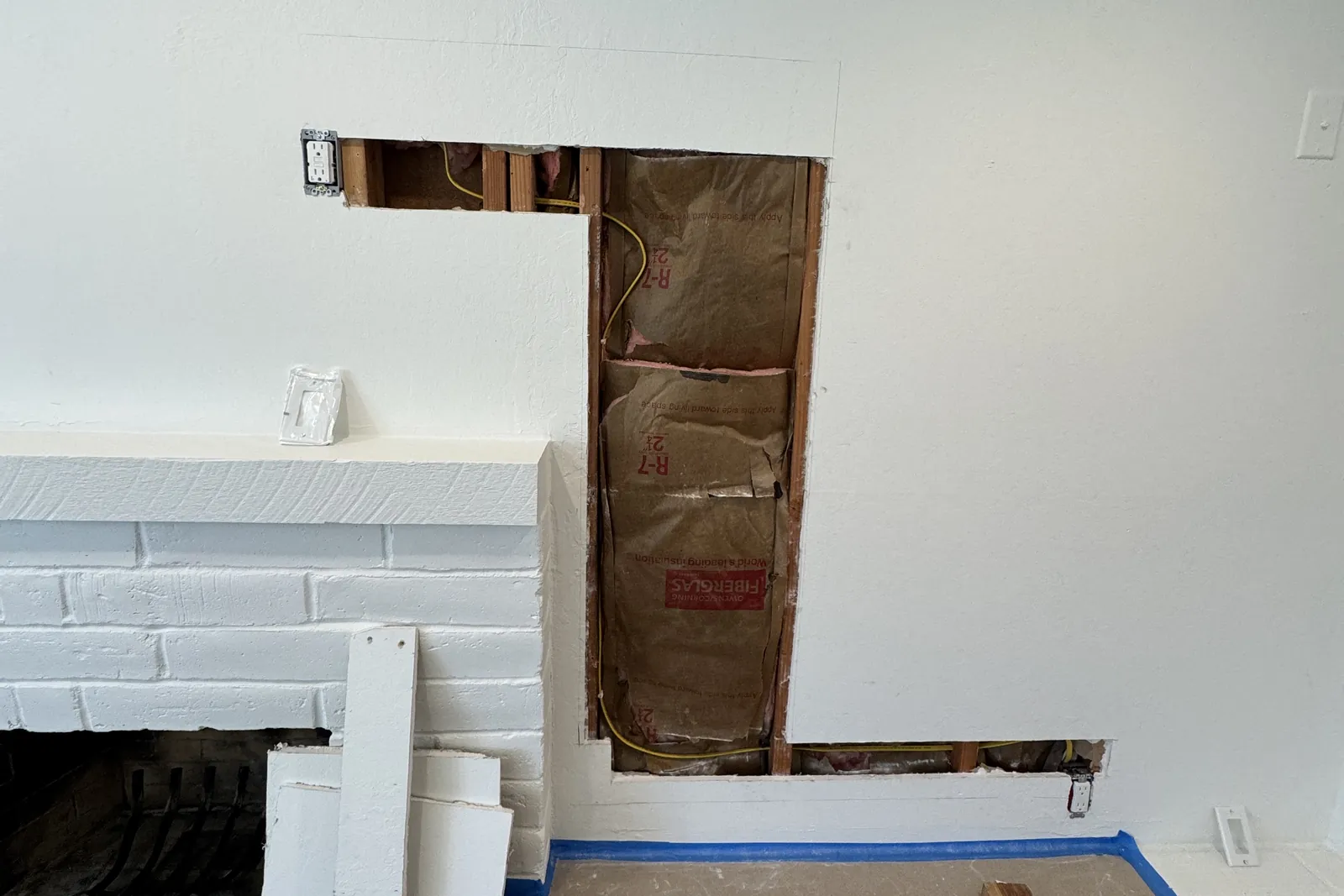 Living room wall opened next to a fireplace to run wiring for a new TV outlet