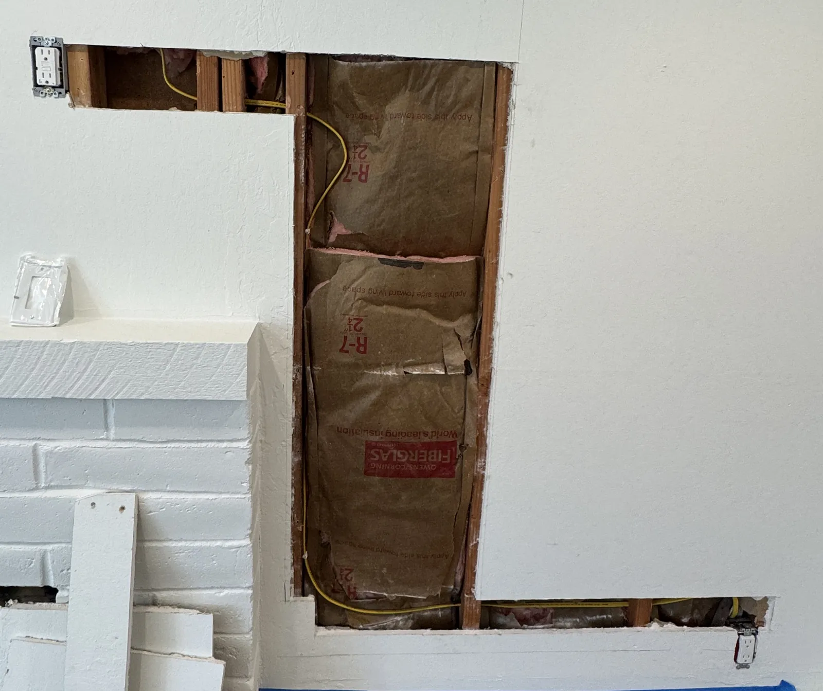 Drywall opened along the route of a new outlet circuit, with the yellow cable running through wall studs and insulation
