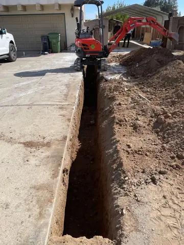 Compact red excavator beside an open trench through a residential driveway