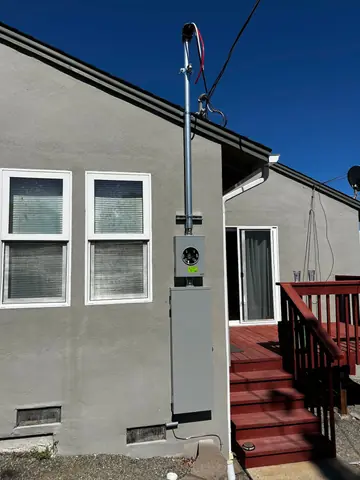 Electrical meter enclosure and vertical service mast on a house exterior