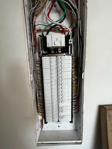 Open indoor electrical panel with rows of breakers and labelled circuit wires
