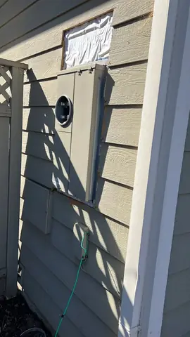 Electrical meter and vertical service mast beside the corner of a house