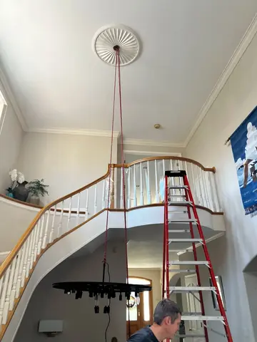 Interior stairwell with a ceiling light fixture and ladder; a person is partly visible at the lower edge