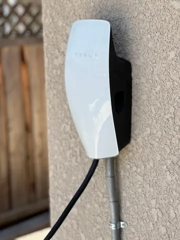 White Tesla Wall Connector and metal conduit mounted on an exterior stucco wall