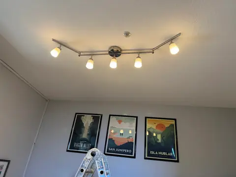 Five illuminated adjustable ceiling spotlights above framed wall prints